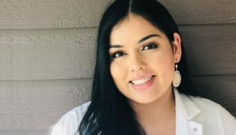Woman with black hair wearing a lab coat smiling.