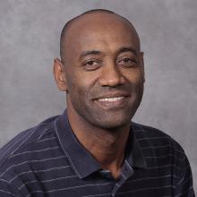 Man wearing a black striped shirt smiling.