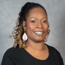 Woman with ombre pulled-back curly hair wearing dangling earrings and a black top 