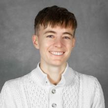 Person with short brown hair wearing a white cable-knit sweater