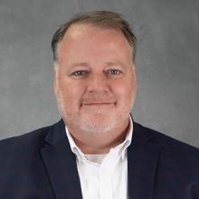man with short brown hair and close cropped graying beard wearing navy blazer and white shirt