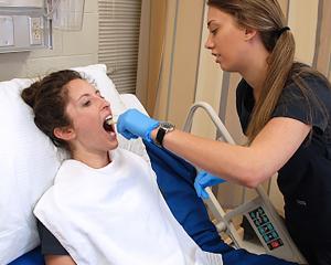 2 individuals in a medical setting, one on a hospital bed and one conducting a health-check up