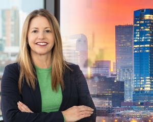 Woman with brown hair wearing a green shirt and blue jacket. Denver skyline in the background.