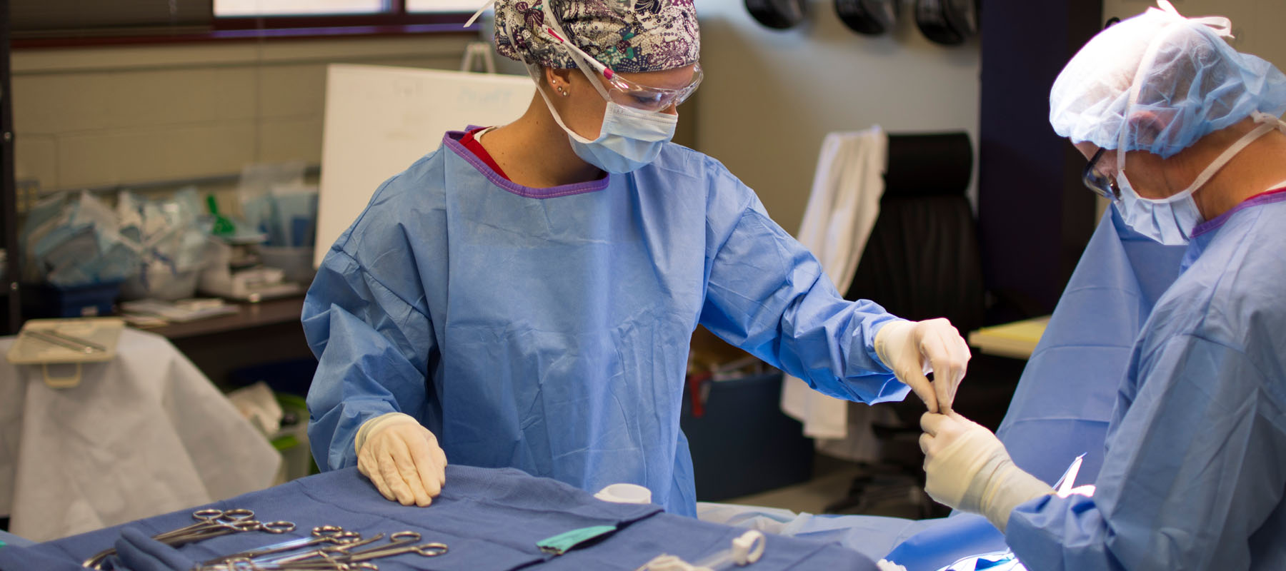 person in protective gear hands medical instrument to surgeon