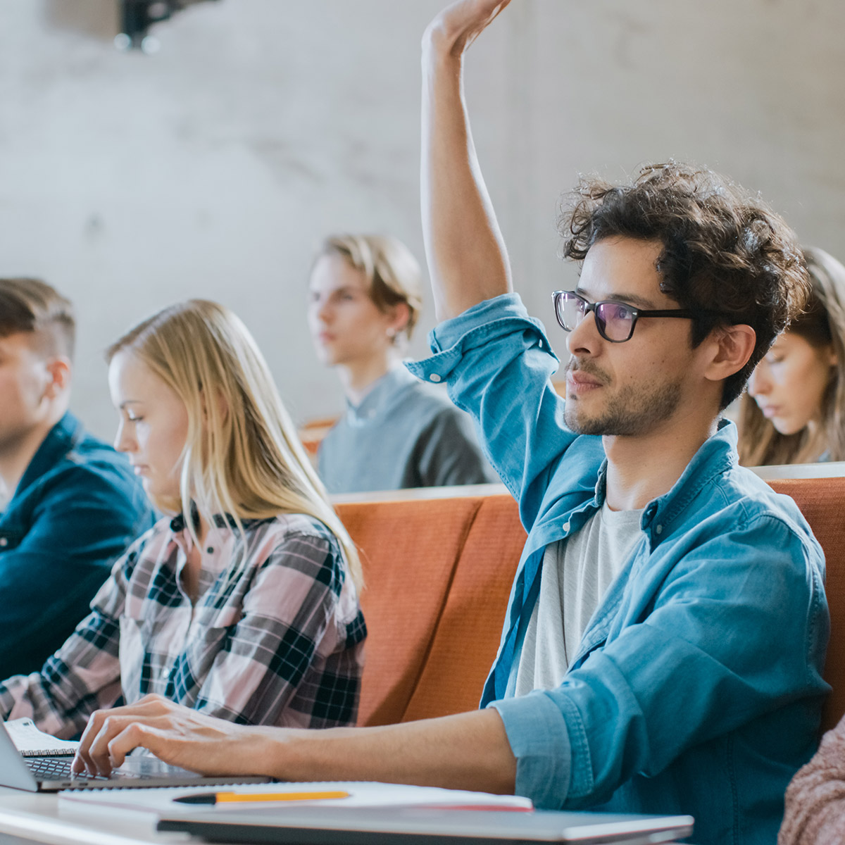 male student in classroom with hand raised