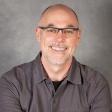 Man with short beard and hair wearing glasses and a gray shirt