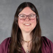 woman with long brown hair wearing glasses and purple top