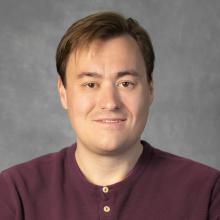 Man with sort brown hair wearing a maroon shirt
