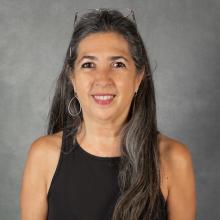 Woman with long salt & pepper hair wearing a sleeveless black top