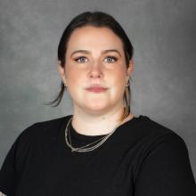 Woman with pulled back dark hair wearing a black top and gold necklace