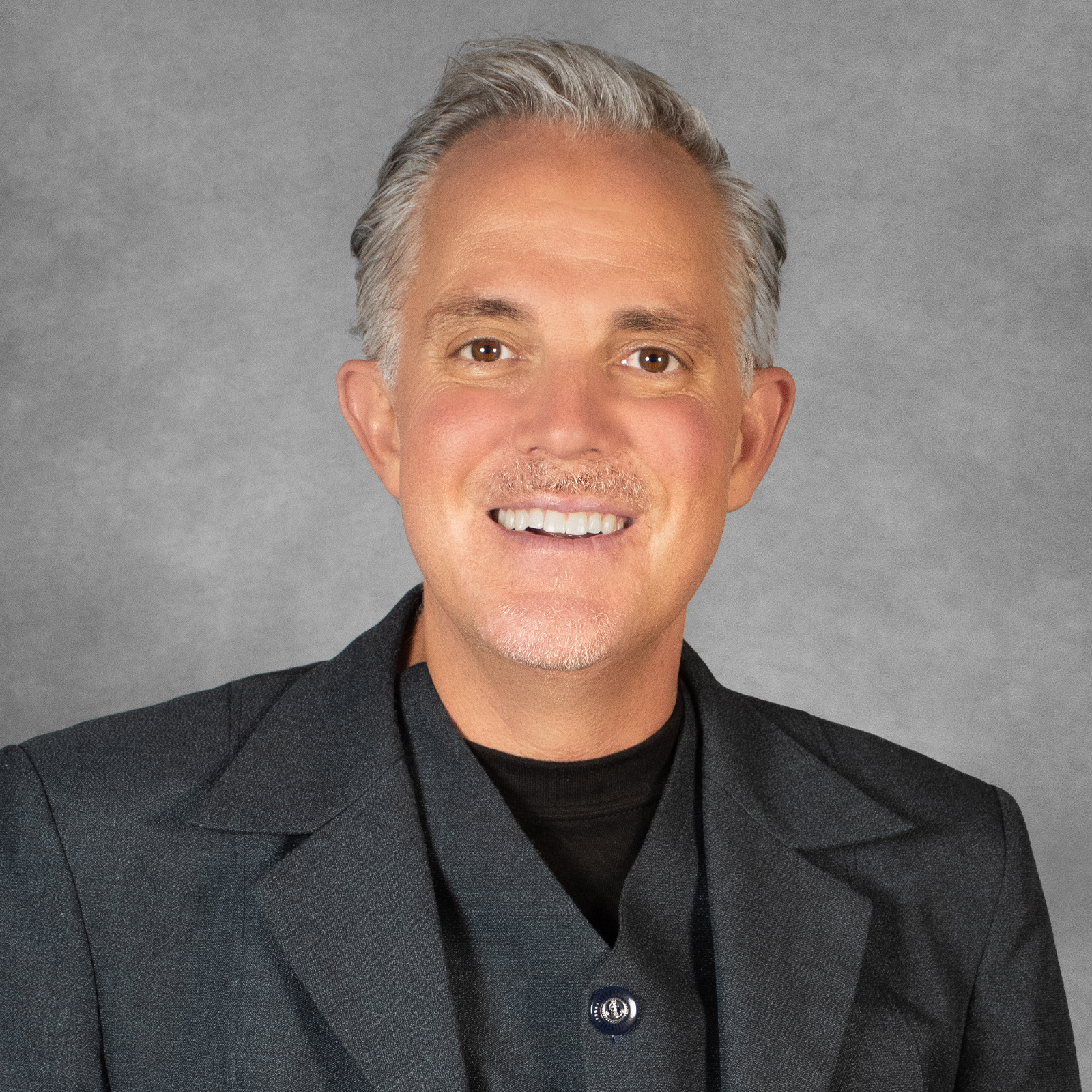 Man with short gray hair wearing a dark gray suit