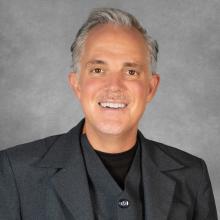 Man with short gray hair wearing a dark gray suit