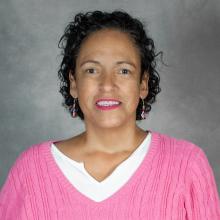 Woman with curly dark hair wearing a bright pink sweater over a white top