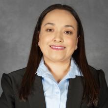 Woman with long dark hair wearing black jacket with light blue collared shirt